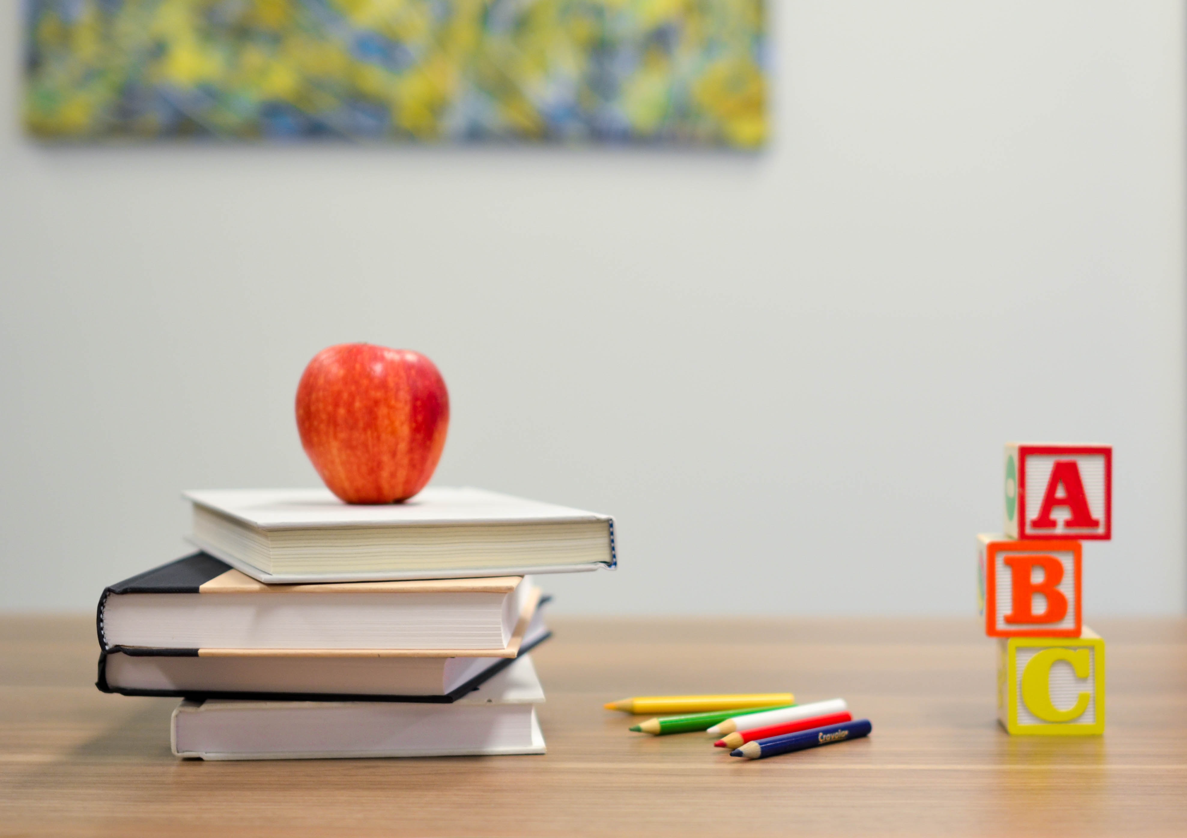 Edukacja - obrazek przedstawiający trzy książki, jabłko, kredki oraz klocki z literami alfabetu na biurku szkolnym