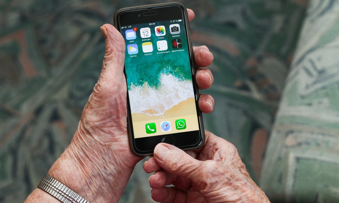Zdjecie przedstawiające dłonie starszej osoby trzymajacej smartfon