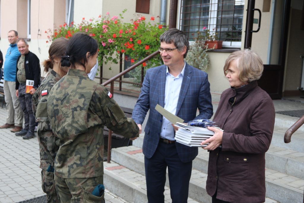Wójt Gminy Tymbark wraz z Dyrektor Szkoły w Tymbarku Jolantą Dunikowską-Wszołek przekazują nagordy dla wóch dziewcząt, które ubrane są w wojskowe mudury.