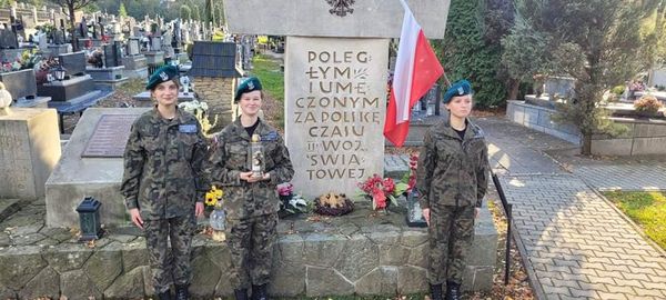 trzy dziewczyny w wojskowych mundurach przy mogile poległych na cmenatrzu.