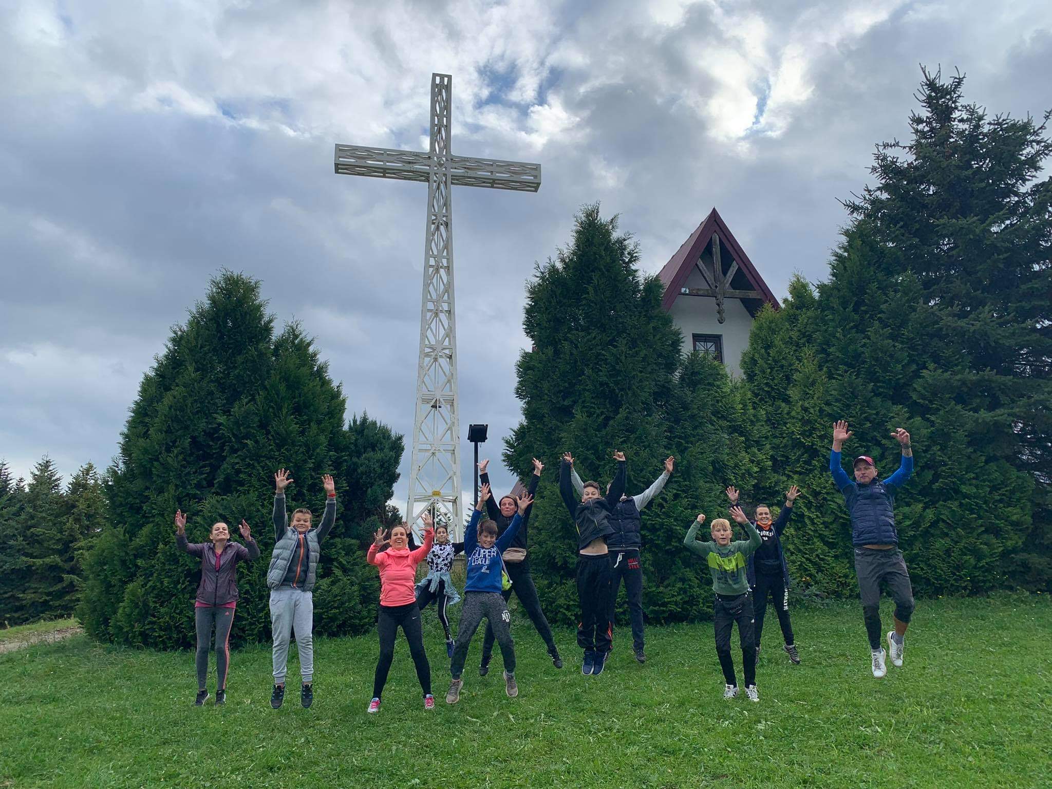Młodzież na uczycielami skaczą na tle krzyża na górze Paproć.