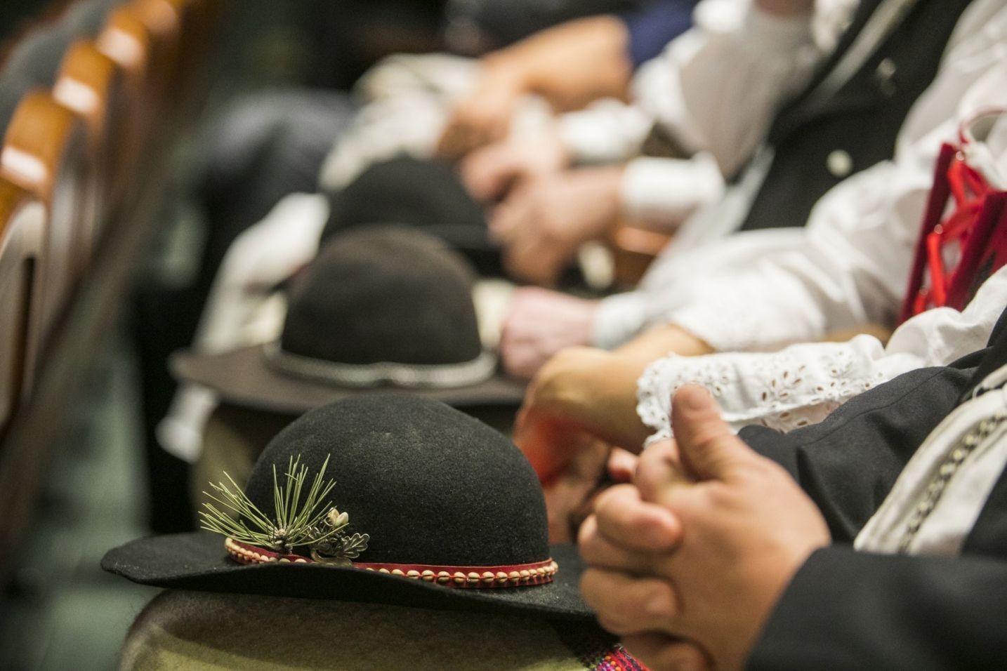 zdjecie przedstawiajace zbliżenie na grupę siedzących osób w strojach góralskich - mężczyźni z kapeluszmi góralskimi na kolanach