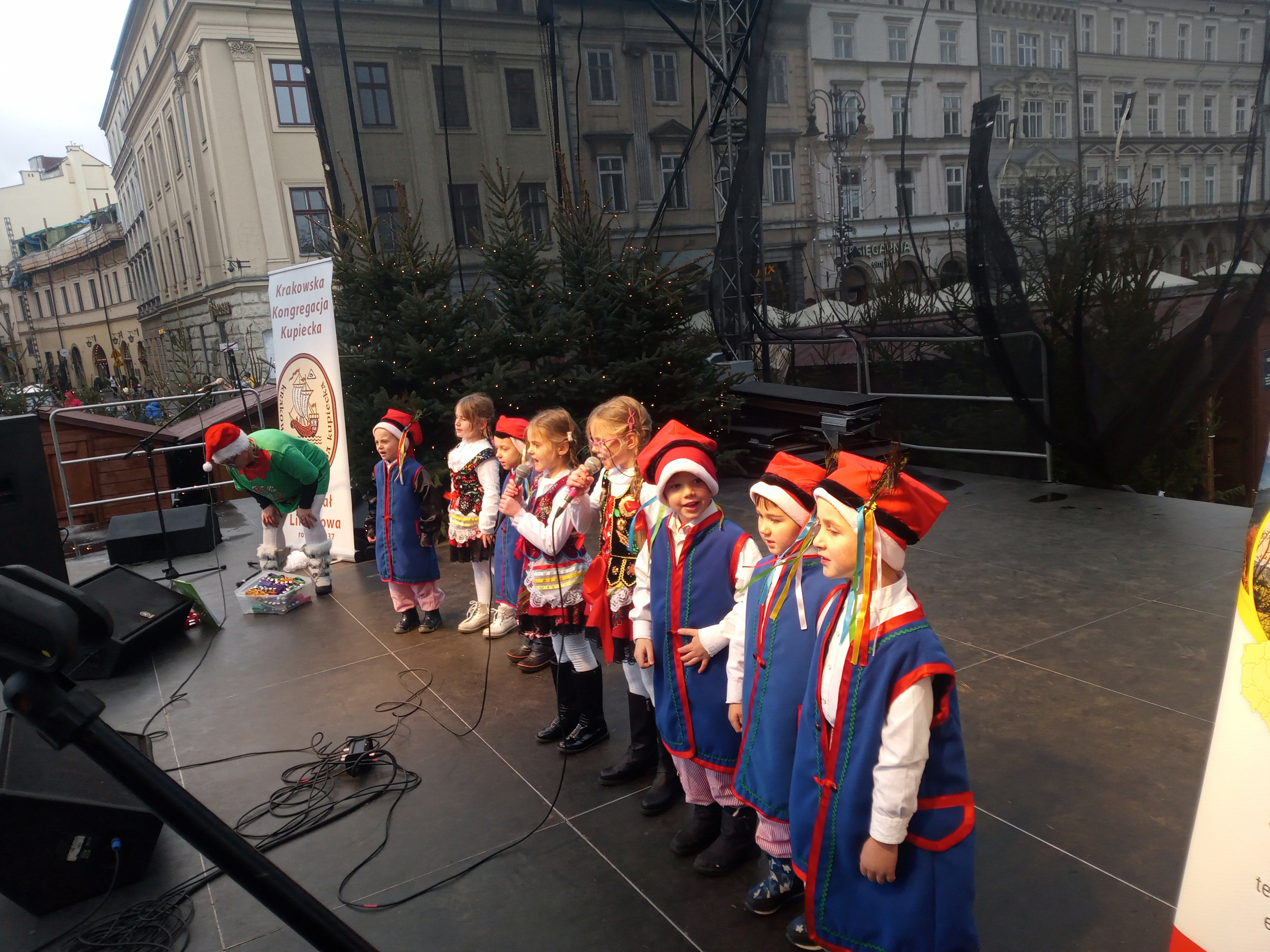 Zdjecie przedstawiajace grupę dzieci w krakowskich strojach ludowych podczas występu na sceie