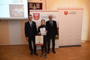 dziewczynka trzyma dyplom i nagrodę, obok stoją starosta i W. Włodarczyk