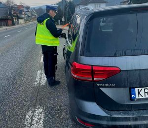 policjant w kamizelce odblaskowej daje opaskę odblaskową kierowcy grafitowego samochodu