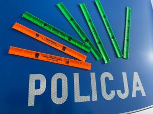 opaski odblaskowe w kolorze pomarańczowym i zielonym na niebieskim tle z napisem policja
