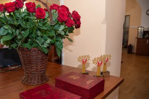 wiklinowy kosz z różami, dwa stosy listów gratulacyjnych oraz trzy statuetki powiatu