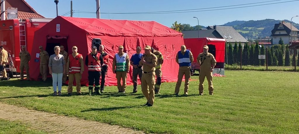 wicestarosta i strażacy w żółtych mundurach obok czerwonego namiotu