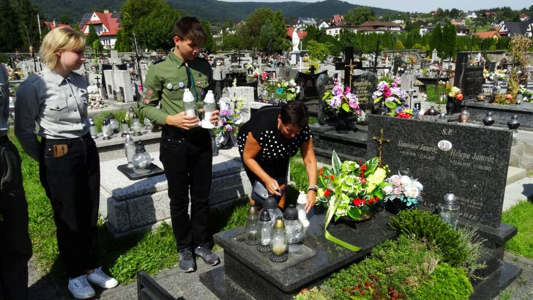 dyrektor Agnieszka orzeł zapala znicz na grobie, obok stoją harcerze