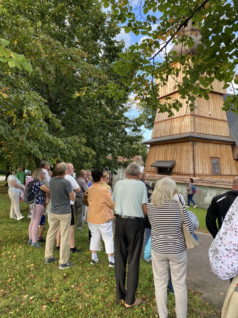 ludzie stoją przed starym drewnianym kościołem w Skrzydlnej