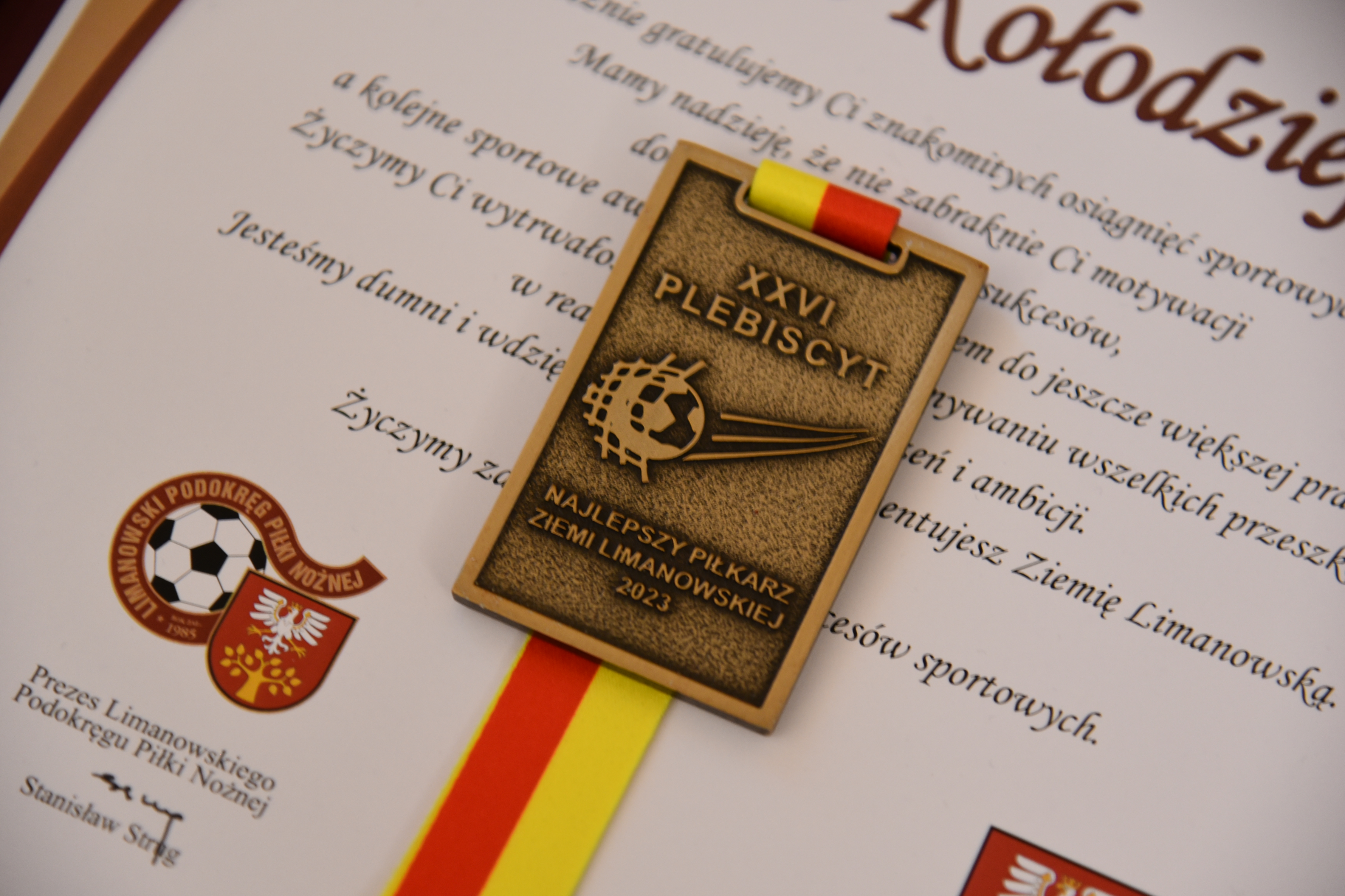 medal z żółto-czerwona wstęgą na tle listu gratulacyjnego
