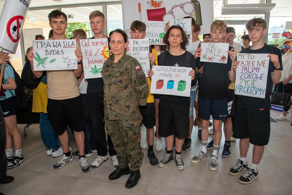 grupa chłopaków trzyma plakaty z hasłami, przed nimi stoi żołnierka w moro